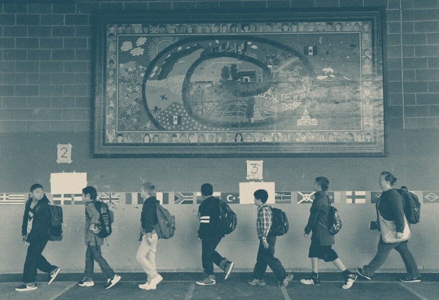 Students with backpacks walk past a hallway mural and a row of world flags.
