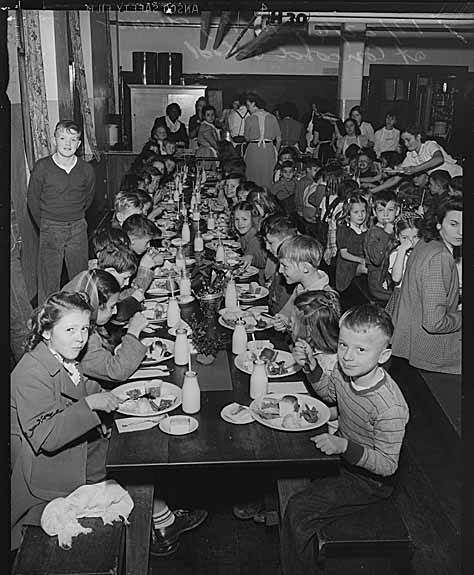 The lunchroom at midday: students at long tables with glass milk bottles.